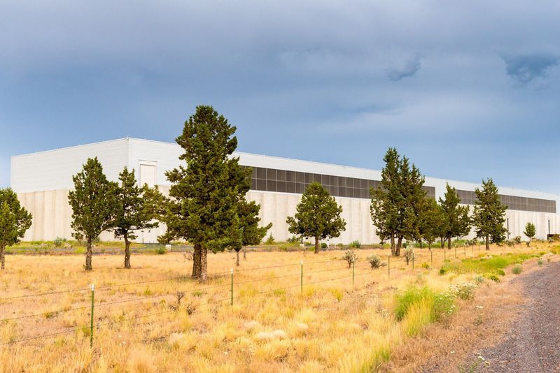Centro de datos de Facebook, hoy Meta, junto a la carretera 126 al oeste de Prineville, Oregón, con pinos y pasto seco en primer plano