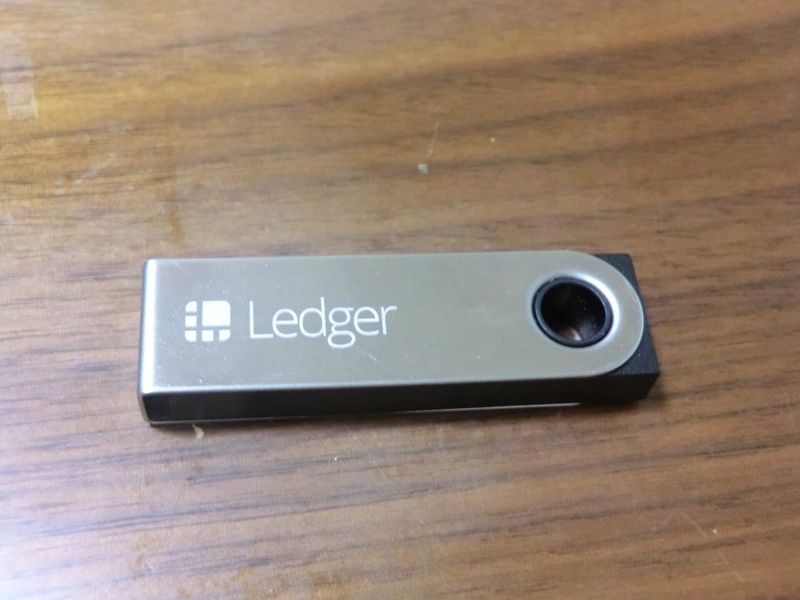 Monedero físico de criptomonedas de la marca Ledger, distinta de Keystone, apoyado sobre una mesa de madera