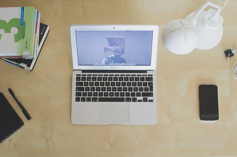 Portátil abierto sobre un escritorio claro, junto a un teléfono, una lámpara y unos cuadernos